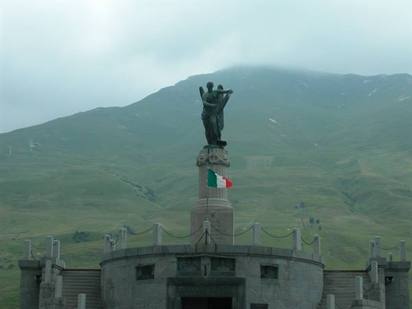 Bronze statue on stone pedestal with tricolor flag, green mountains in mist