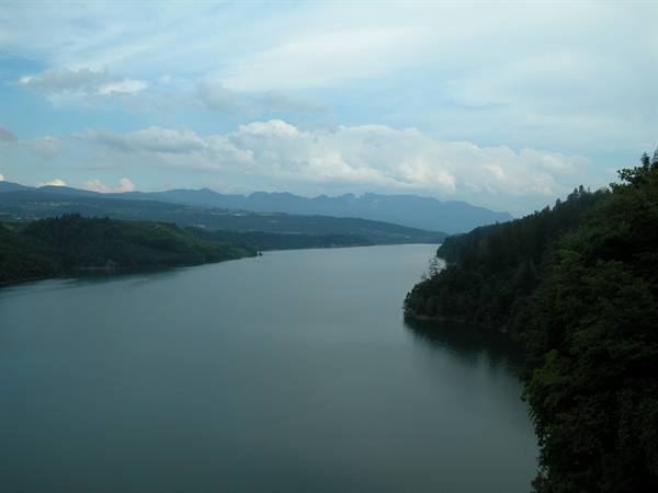 Lago Suviana: calm water between green woods and hills under clouds