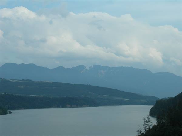 Calm lake beneath white clouds, dark forests and blue mountains in the distance