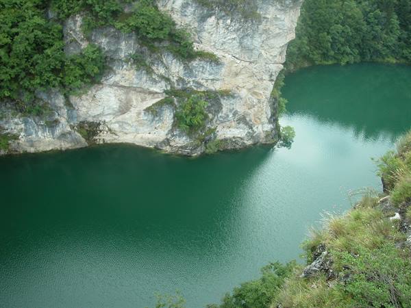Green lake enclosed by limestone cliff and dense forest, soft daylight