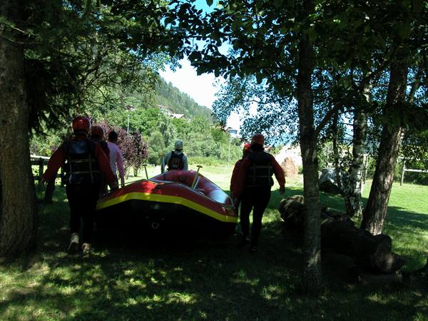Group in helmets and life jackets carrying a red and yellow raft through trees