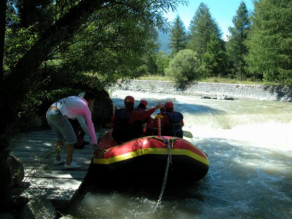 Red inflatable raft with helmeted paddlers launching into a rapid river