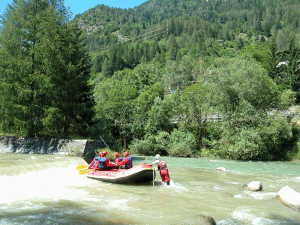 Rafting group in red raft descending rapids among green trees