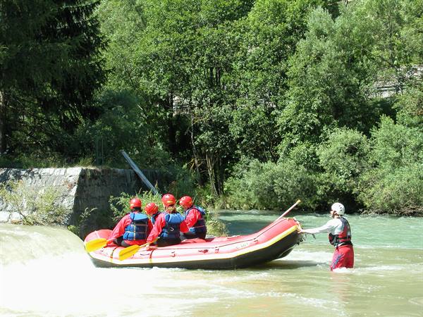 Group in red helmets rafting on green river, guide standing in water