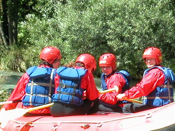 Four people in red helmets and blue vests paddling a red raft