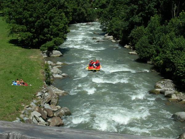 Yellow raft with people in red descends a rushing river between rocks and green meadow
