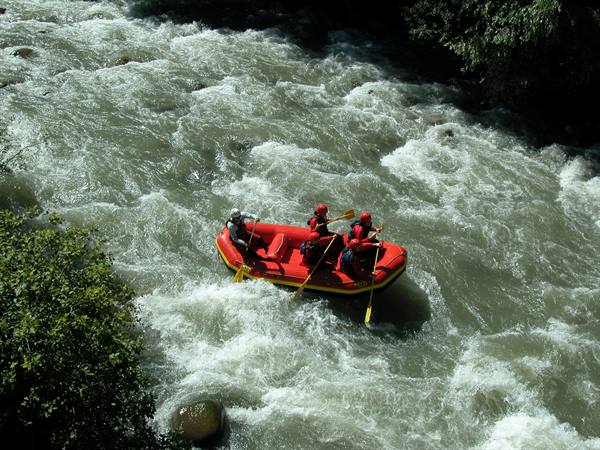 Group in red helmets rafting a red inflatable boat through foamy rapids