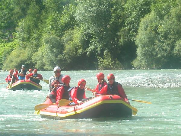 Rafters in red helmets paddle yellow and red inflatable boats down the green river