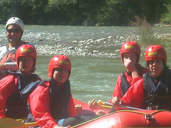 Group in red helmets and jackets paddling an inflatable raft on a green river