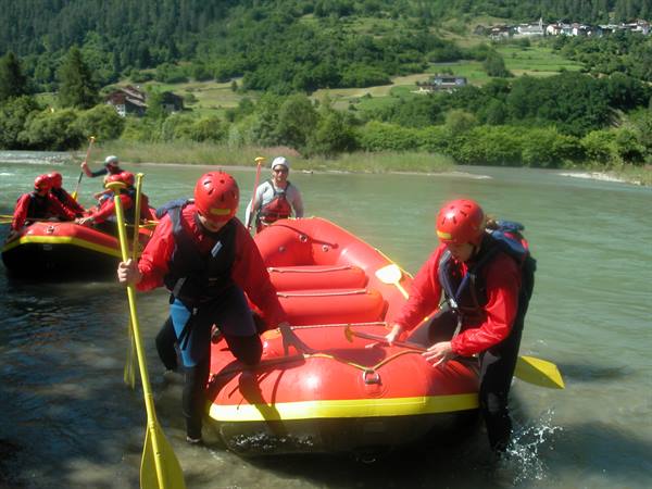 Rafters in red helmets drag yellow and red rafts into the alpine river