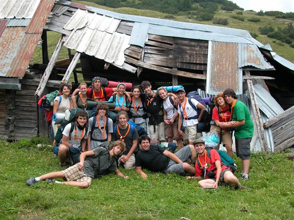 Group of hikers with backpacks in front of a rundown wooden cabin