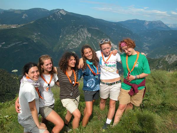 Six scout girls hugging on a mountain meadow, green peaks in the background