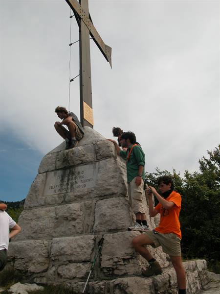 Scouts in orange and green shirts climbing stone summit base with metal cross