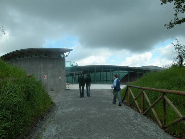 Visitors walk toward a modern glass and concrete building under cloudy skies