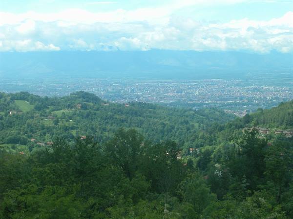 Green hills with scattered houses and a distant city under clouds