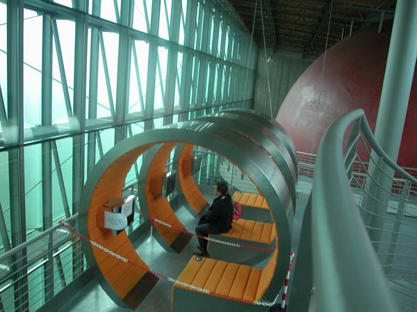 Visitor sitting on orange circular pods beside the glass windows of a museum