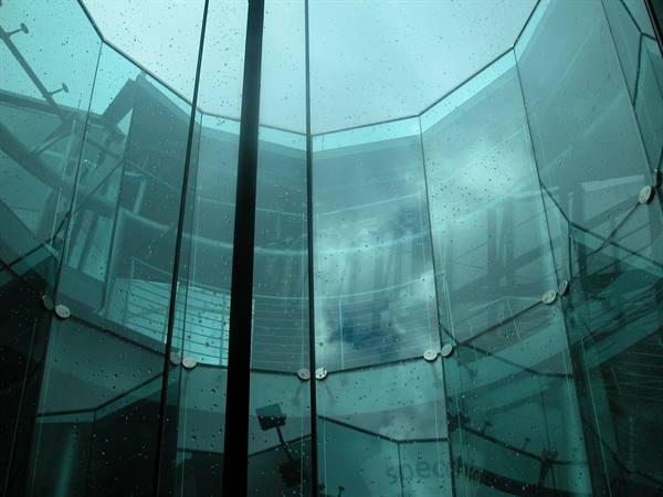 Curved green glass walls with raindrops and cloudy sky reflections