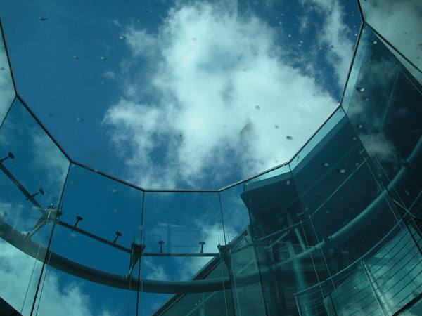 Transparent glass ceiling with white clouds and metal structures reflected