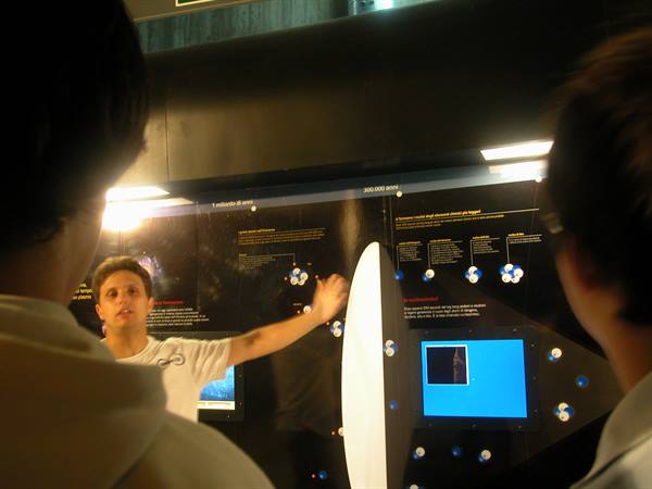 Boy points at a dark exhibit panel with blue screen in a museum