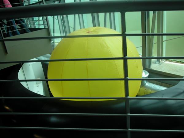 Yellow inflatable sphere inside a black structure, seen through a metal railing