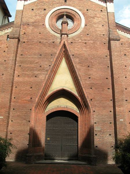 Red-brick Gothic church facade with pointed arched portal and round window, daylight
