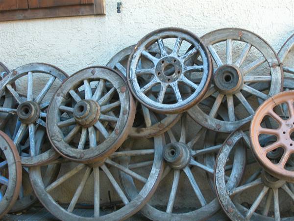 Vintage wooden wagon wheels stacked against a white daylight wall