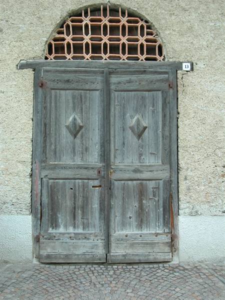 Old grey wooden double door with terracotta fanlight, plastered wall, cobblestones