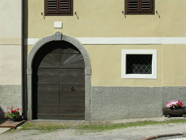 Dark wooden arched door on yellow facade with brown shutters
