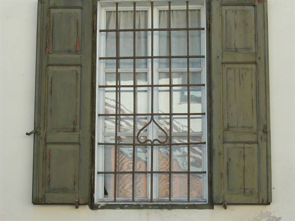 Window with wrought iron grille and faded green shutters on white wall