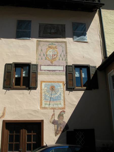 Frescoed facade with painted sundial, heraldic crest and dark wooden shutters
