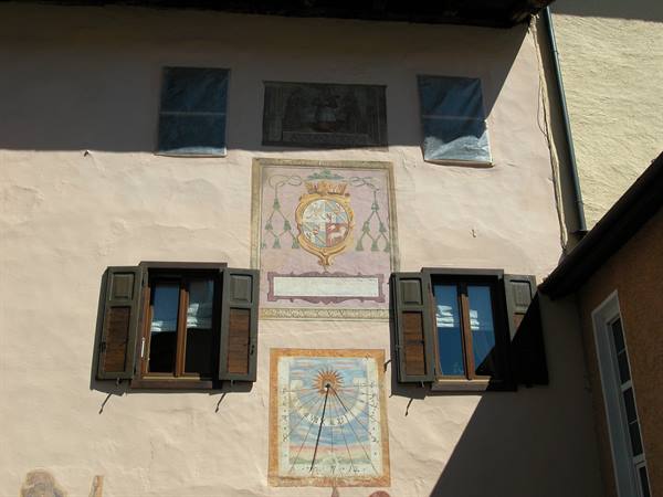Pink facade with painted sundial, frescoed coat of arms and wooden shuttered windows