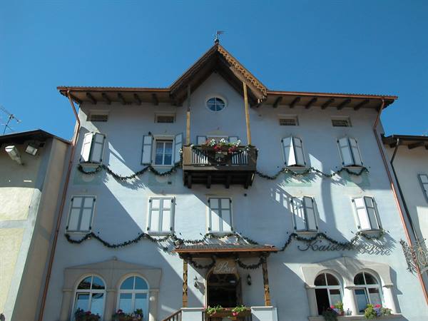 White Tyrolean hotel facade with wooden balcony and geraniums under blue sky