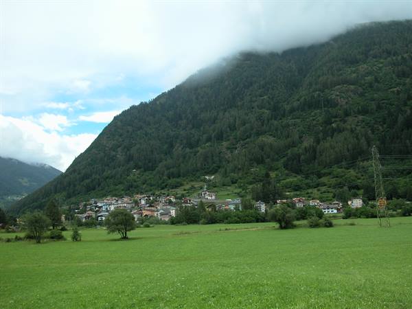 Village beneath forested slope, low clouds over the mountain