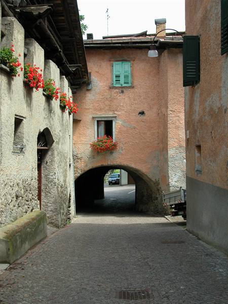 Cobbled alley with arch under pink house, red geraniums on windows