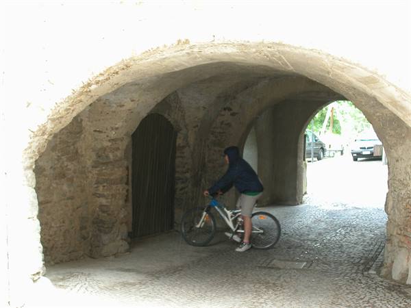 Boy on a bicycle under an old stone arch with wooden gate