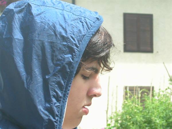 Boy in blue rain hood in front of house with shutters
