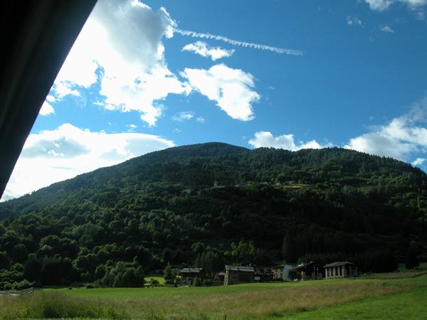 Wooden houses village beneath a forested mountain, blue sky with clouds