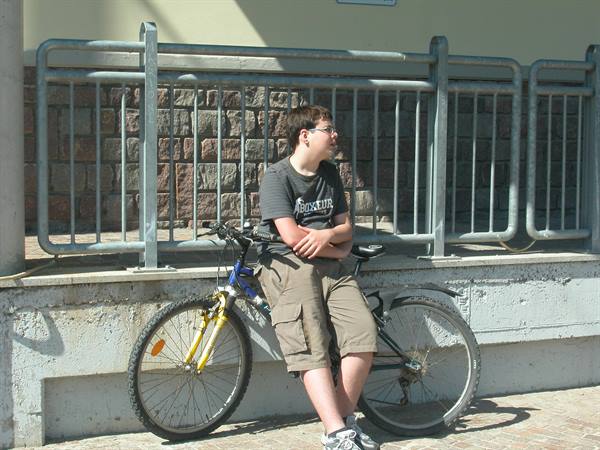 Boy with glasses leaning on a blue mountain bike in front of a metal railing