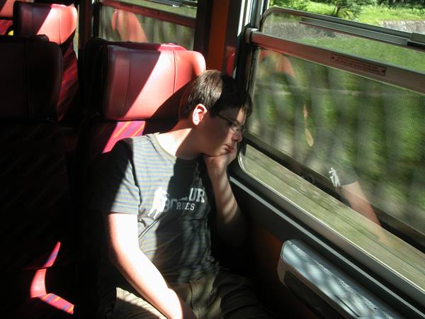 Boy with glasses asleep on red train seats, sunlight on the window
