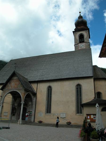 Church with bell tower and frescoed porch, people walking across the cobbled square