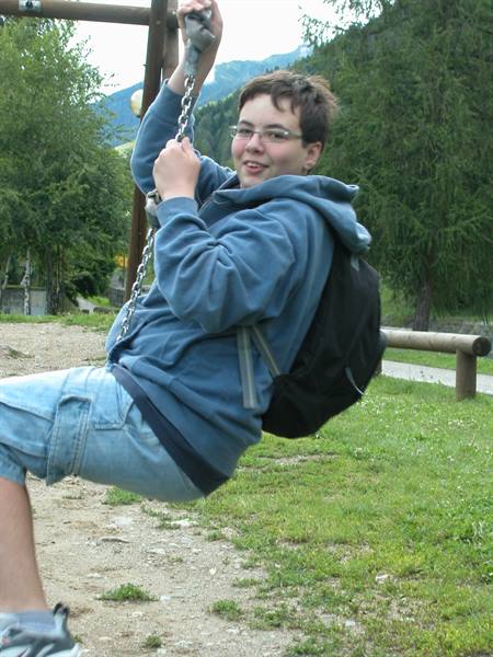 Boy with backpack on a chain swing in a green park
