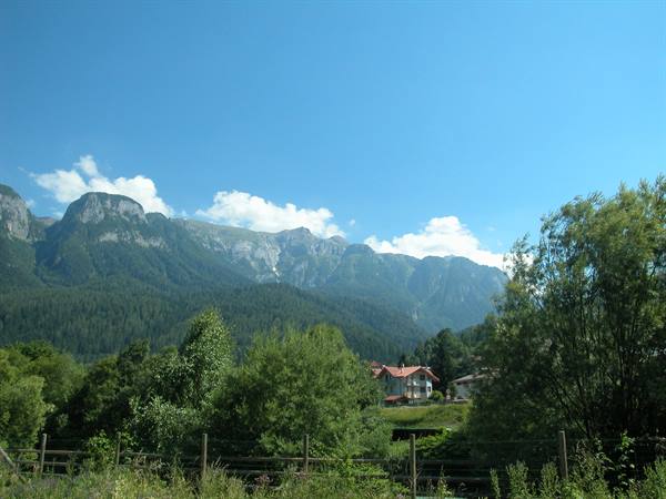 Red-roofed house among trees beneath rocky Dolomite peaks