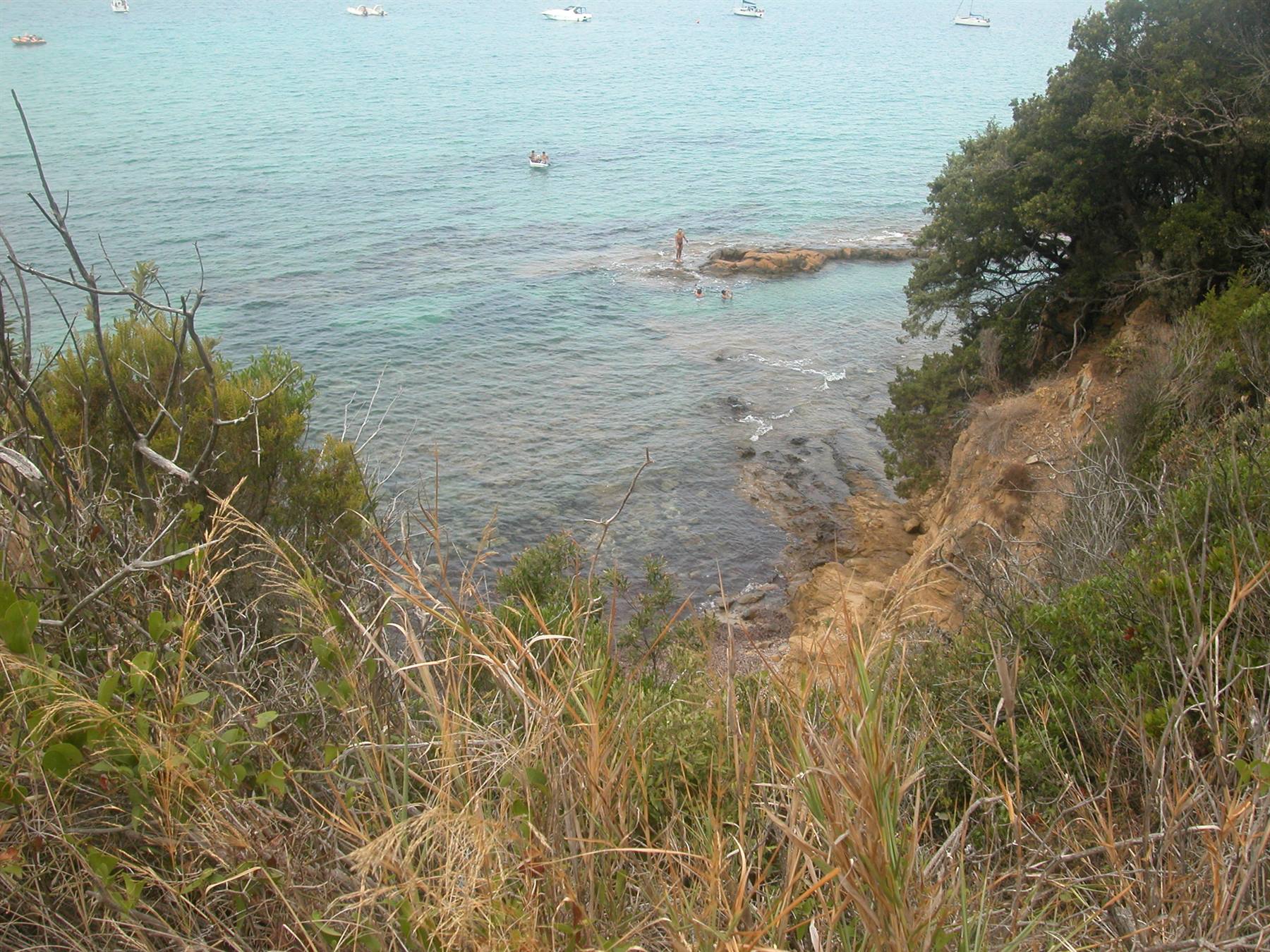 Turquoise bay with rocks, moored boats and a swimmer on a rock