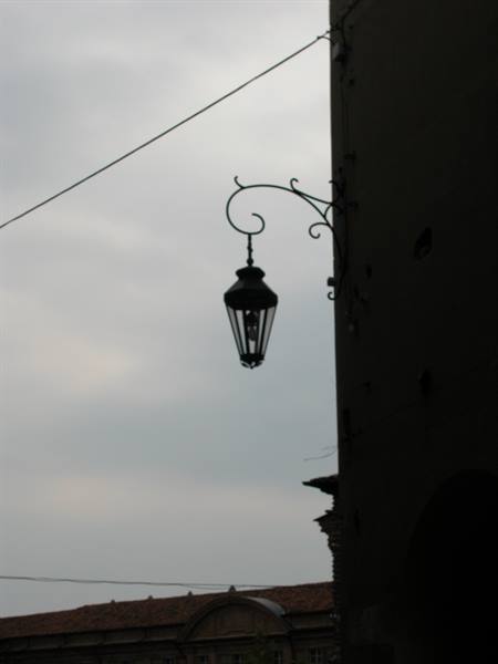 Black wrought-iron lantern hanging from dark building against gray sky