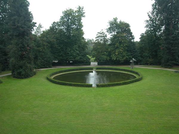Circular reflecting pool with central fountain, green lawn and dense trees
