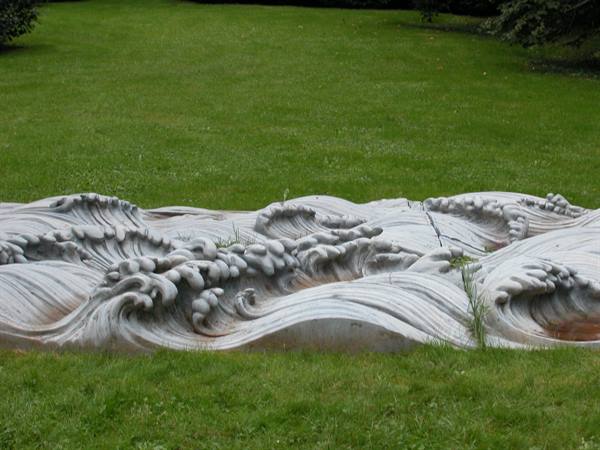Marble sculpture shaped like ocean waves on a green lawn