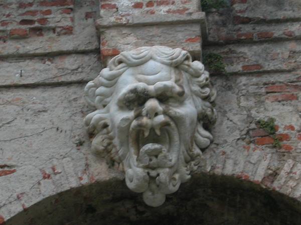 Baroque marble screaming mask above a brick archway