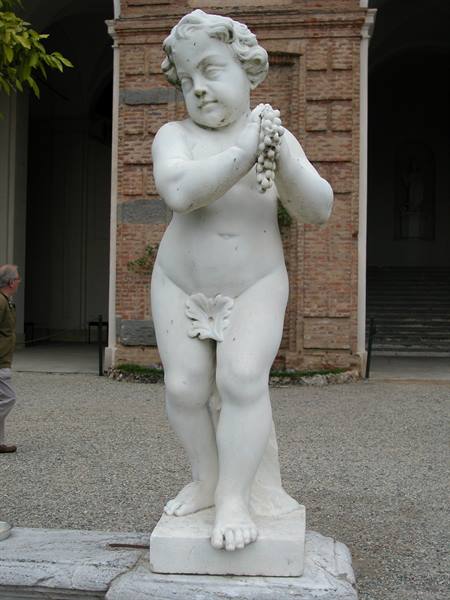 Marble statue of a cherub holding a grape cluster in front of a brick building