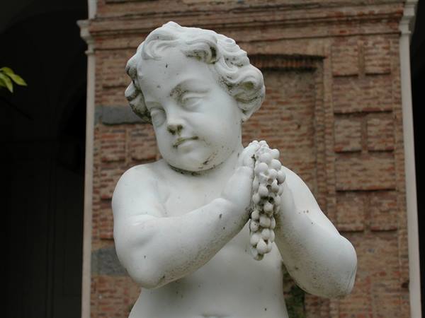 Marble statue of a cherub clutching a bunch of grapes against a brick wall