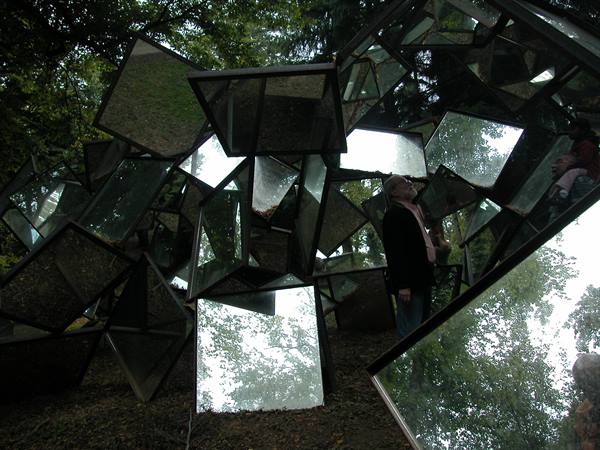 Man among mirror sculptures reflecting trees in the woods